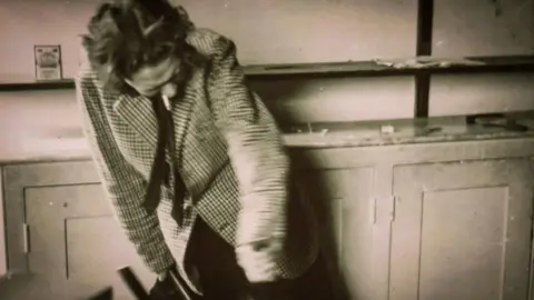 Jeff Towns Dylans Bookstore Dylan Thomas in a black and white photo his head down and cigarette in the of this mouth. He is hunched over a bit and still still twisting something unseen with his arms.