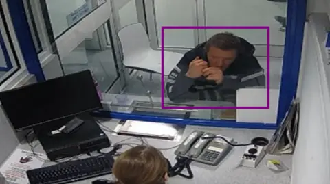 The CCTV images of the Essex Police show Mark Donovan bowing with the elbows at a counter at the Ilford Police station. He wears a coat and looks through a glass pain to a police personnel member.