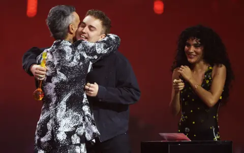 Sam Fender receives an award for Song of the Year from Robbie Williams, next to Olivia Dean during the BRIT Awards at the Co-op Live Arena, in Manchester. 