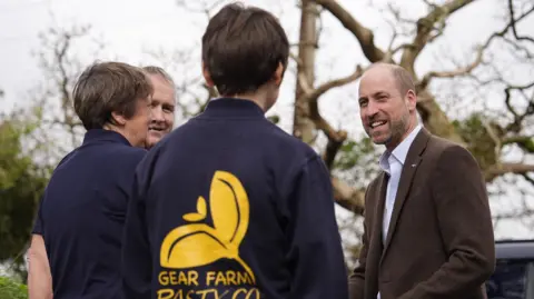 A picture of William speaking with workers at Gear Farm Pasty company. He is wearing a brown suit jacket.