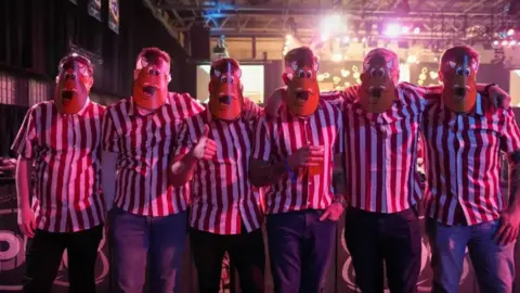 City of Wolverhampton Council Six people wear facemasks and stripey shirts at the darts event. The masks evokes memories of Bully, the character from TV quiz show Bullseye, which began in the 1980s.