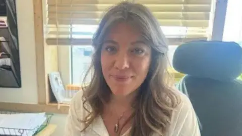 Dr Jessica Langtree Marsh is pictured in her office, she is wearing a white top and has brown hair. 