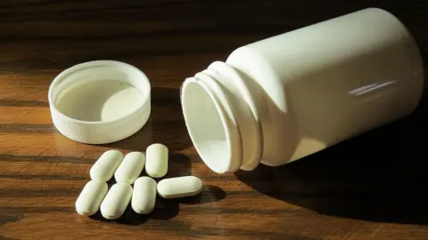 Close-up of a bottle of white pills, with the lid off, lying on a table