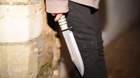 A generic photo of a young man holding a large knife in his right hand