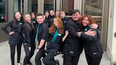 Theatre staff in all black posing outside as a group outside of glass theatre doors