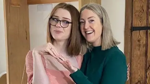 Handout Brianna Ghey, with straight reddish-brown hair and wearing a pink top and glasses, poses with her mother Esthey Ghey, who has shoulder length blonde hair and is wearing a green jumper. 