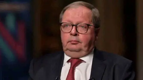 Andrei Kelin in a red tie sits in a dark room