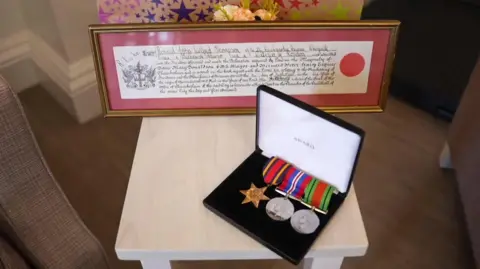 Richard Knights A small square table with a smart black box displaying three medals. There is also a framed page in calligraphy that is some kind of presentation to Ron.