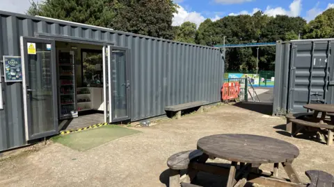BBC Grey temporary container buildings and round wooden table on a sunny day. 