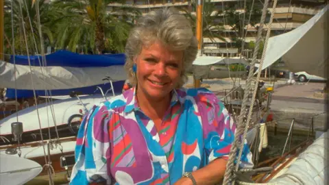 Getty Images Judith Chalmers in a bright multi-coloured blouse in front of a Mediterranean harbour on Wish You Were Here?