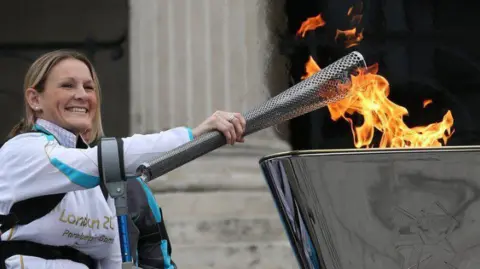 Getty Images Claire Lomas holds a flaming torch over a steel cauldron