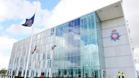 PA Media An outside view of Greater Manchester Police headquarters, a modern style office building with grey cladding and a GMP flag being flown outside