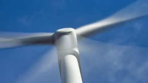 Getty Images A wind turbine in close up with its blurred arms due to the speed of their movement against a blue sky