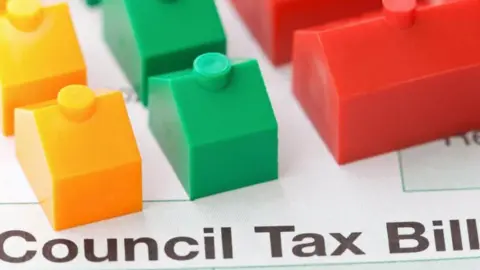 A council tax bill with three Monopoly style houses on top of it, one yellow, one green and the other, a larger one, red  