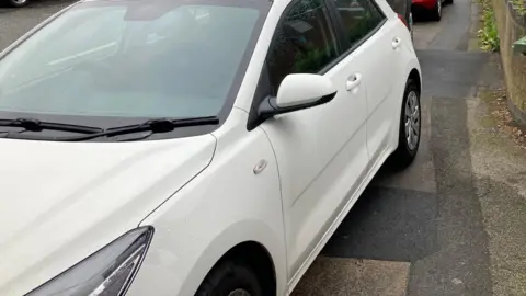 BBC A white car parked on a pavement.