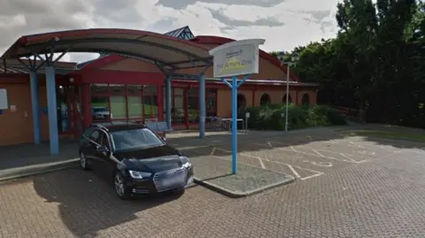 A sign outside of the Activity Zone leisure centre that says "activity zone". The building looks dated and there is a black car parked outside the entrance.