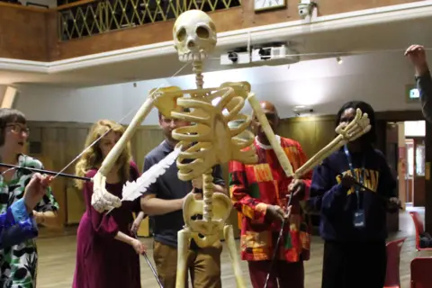 Paul Fitzgerald A group of five people animate a giant puppet depicting the skeleton of Thomas Paine