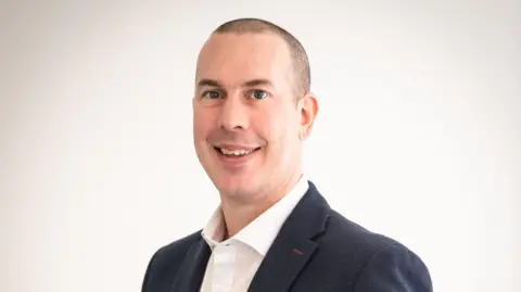 Abri Sam Stone from Abri smiling at the camera in a professional photo against a blank background