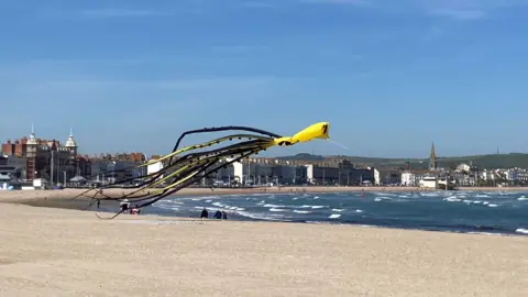BBC Weather Watcher Brownowl Weymouth Beach - a large yellow and black kite flying over the sand with the sea to the right.