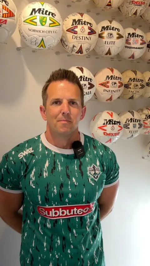 Simon Francis is stood at the top of his stairs wearing a green with black and white stripes and smiling straight at the camera. 