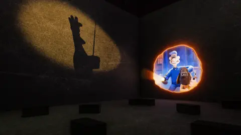 Justin Sutcliffe A image of Wallace and Gromit at the exhibition. Wallace is wearing a blue uniform and holding a torch. Gromit is wearing a mask and holding a blow torch. Opposite the duo is the shadow of a chicken holding a radio. 