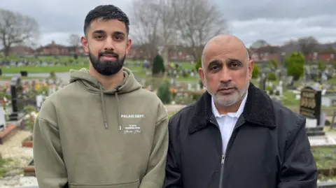 Sahil Hussain and his uncle, Tariq Khan, in front of their relatives grave at Dewsbury Cemetery. They are both looking sad.