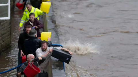Getty Images A line of men empty buckets of floodwater over a wall and into a river in Pontypridd