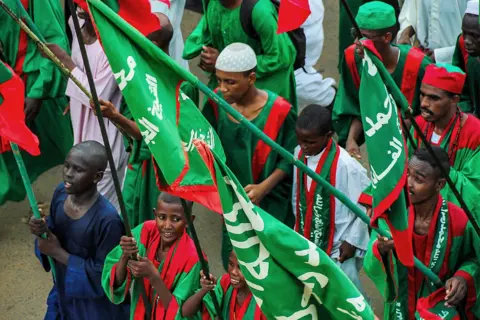 AFP/Getty Images Men wearing primarily red and green hold up flags with Arabic writing on it in Omdurman, Sudan - Saturday 23 August 2025.