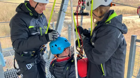 Leanne Rinne/BBC Lord Mackinlay of Richborough being fastened in on his zip wire