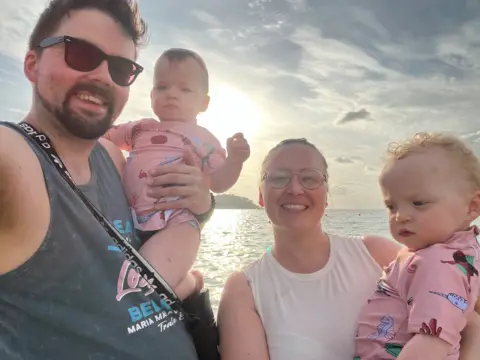 Nathan, his wife and their two children on holiday with a sunset over the sea behind them