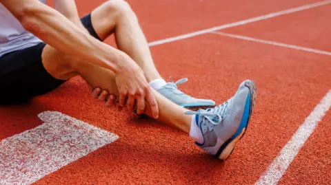 Getty Images Athlete holding his leg injured after running at track and field stadium after jogging, running competition, sports injury concept