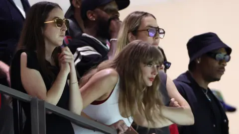 Reuters Taylor Swift, wearing a white vest top, leans over some railings at the Super Dome in New Orleans