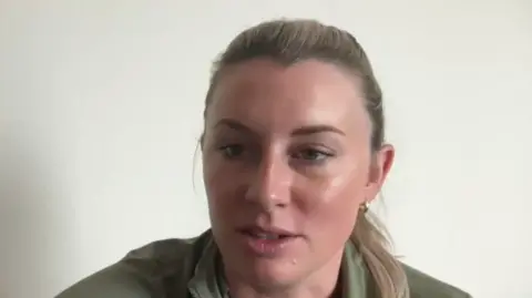 Christi Hill wears a green sweater and has blonde hair