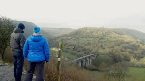 Two people with their back to the camera at the Monsal Trail enjoying a view of the Peak District. 