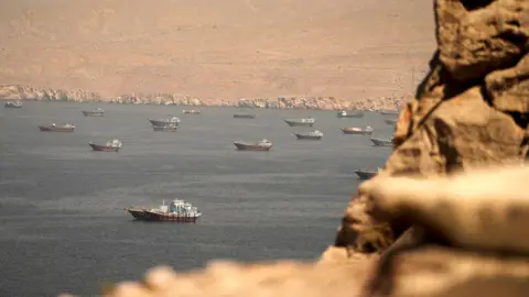 A file photo shows vessels in the straight as pictured from Oman in April, with bokeh Omanian boulders in the foreground and Iranian desert in the background.