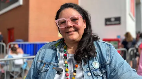 Sabrina has a denim jacket on and colourful beads.