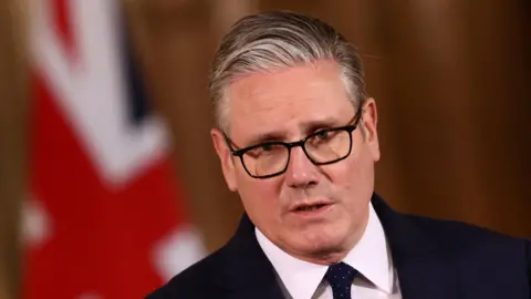Reuters Sir Keir Starmer in a dark suit and tie at a Downing Street press conference, with Union flag backdrop