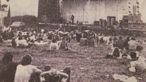 A black and white photo of people sitting in front of a stage.