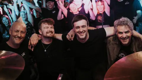 Blue Kid Media Harrison Rimmer (second from left) with bandmates, stood in front of a cheering crowd.