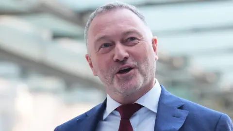 PA Media Environment secretary Steve Reed, wearing a red tie and suit, walks in to BBC Broadcasting House in London, to appear on the BBC One current affairs programme, Sunday with Laura Kuenssberg