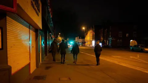 Four women with their backs to the camera walking in Derby city centre at night time. 