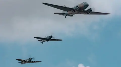RAF Cosford A depiction of the Battle of Britain memorial flight with a Dakota flying alongside a Spitfire and Hurricane against a blue sky. 