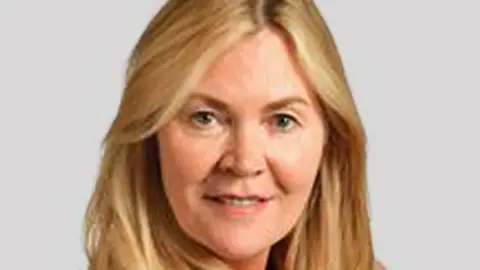 Wirral Council Paula Basnett smiles at the camera. She has long blonde hair and is wearing a pink suit.