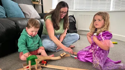 Martin Giles/BBC Erin plays on the floor with a train track with her pre-school son and daughter.