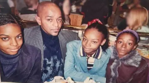 The three sisters, seen as teenagers, and their father sit together at a restaurant table, from left to right, Jane Adetoro, Joseph, Christina Walters and Rebecca Walters.