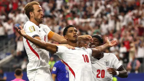 Getty Images Footballers celebrate after scoring a goal. One of them has his hands outstretched and is looking up while two others celebrate around him.