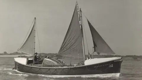 National Historic Ships Registry A black and white image of the Guide of Dunkirk navigating through water. A man is steering the vessel. The vessel has three sails.