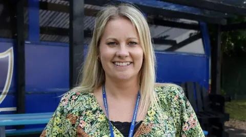 Headshot of Jen Brattan, wearing her lanyard and a colourful dress, with the school's blue book bus in the background.