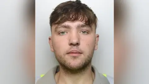South Yorkshire Police Mugshot of Conway who has brown hair and a fringe. He has stubble across his upper lip and along his chin and jaw.