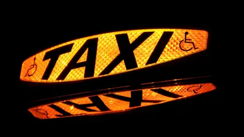Getty Images A yellow light-up sign which says Taxi in black letters. There are also symbols representing a person in a wheelchair. 